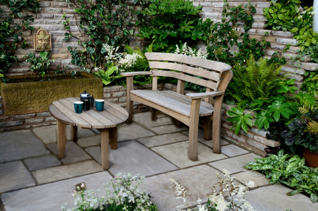 Rustic courtyard garden with a weathered wooden bench, stone paving, and lush green foliage. A cosy and timeless example of courtyard garden ideas for a serene outdoor retreat.