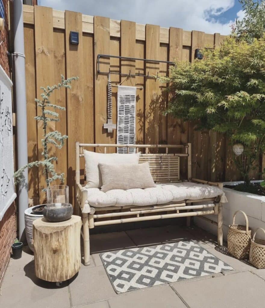 Bamboo garden bench in a small courtyard garden with Japanese acer, log side table and geometric outdoor rug​​​​​​​​​​​​​​​​