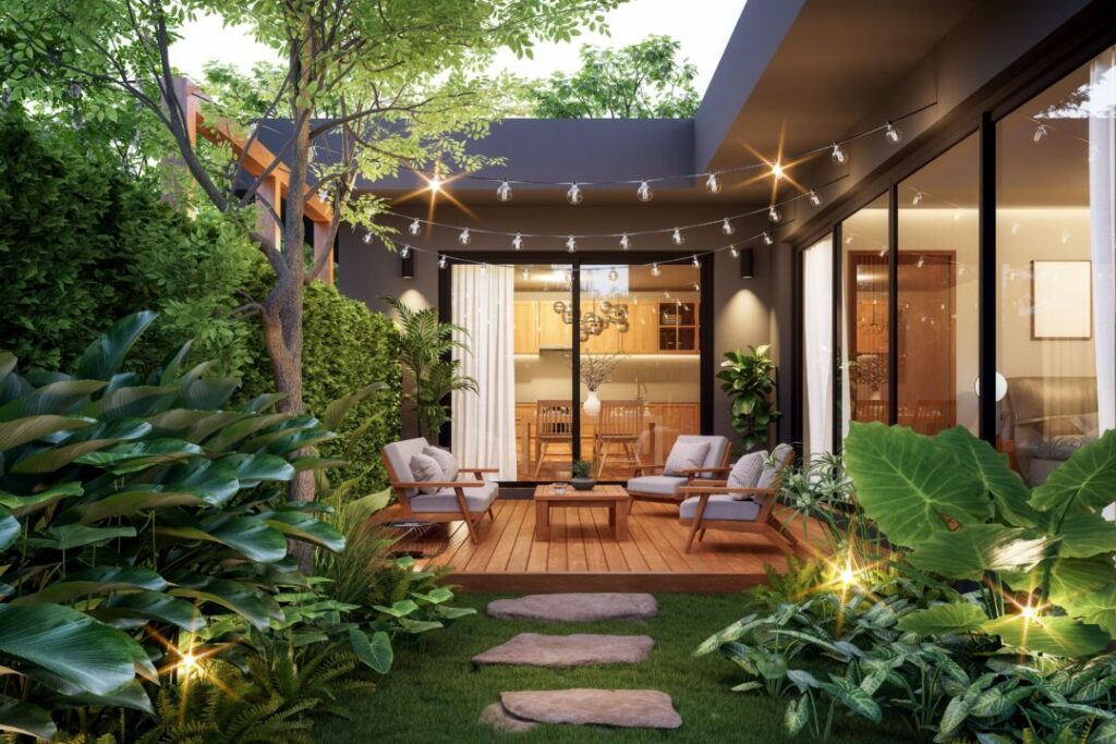 Modern courtyard garden with a wooden deck, lush tropical plants, string lights, and an inviting outdoor seating area. A stylish and cosy example of courtyard garden ideas for evening relaxation.