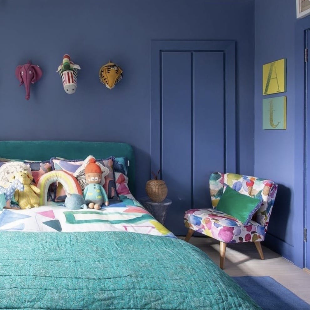Girls bedroom with Farrow and Ball Pitch Blue colour drenched walls, teal bedded and colourful accent chair