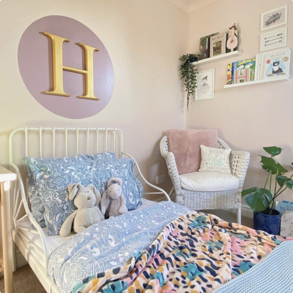 Girls bedroom with Farrow and Ball Pink Ground walls, Cinder Rose painted circle, white iron bed and wicker chair reading corner