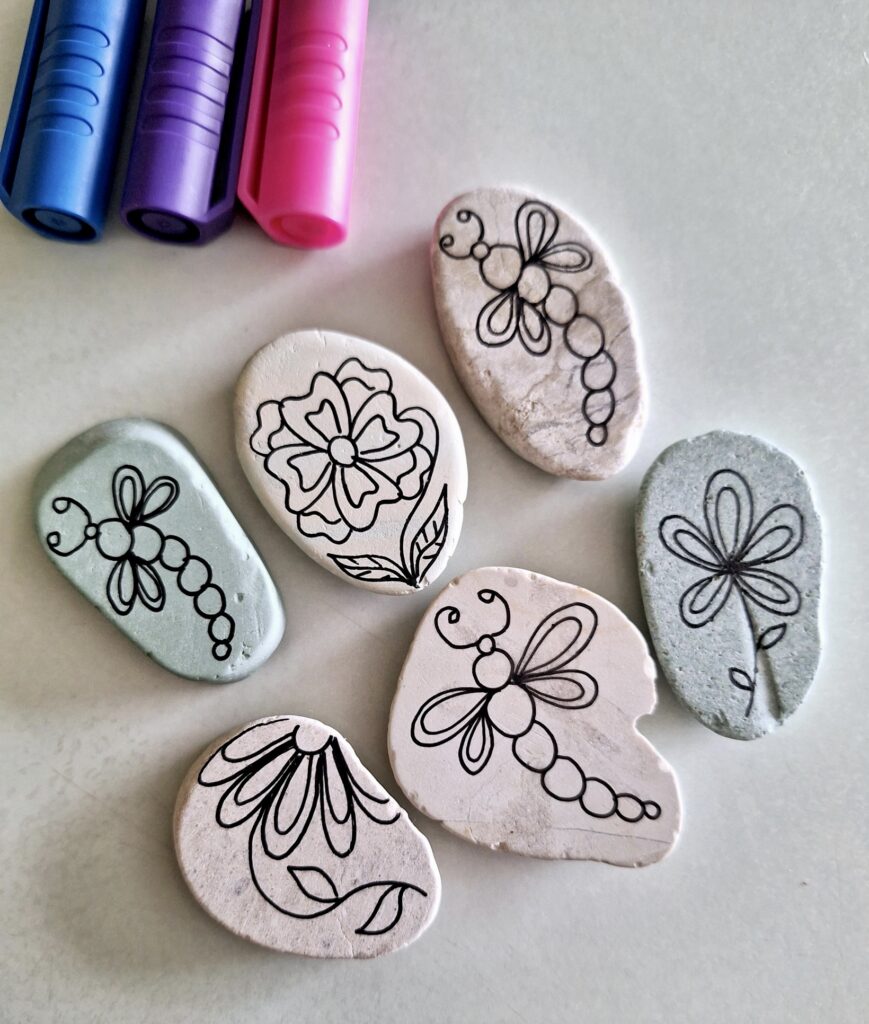 Hand-drawn flower and insect designs on painted stones – an easy and fun summer craft idea for teens.