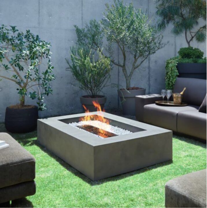 Modern courtyard garden with a sleek firepit table, surrounded by large potted plants and a comfortable modular sofa set. A contemporary take on courtyard garden ideas for stylish outdoor relaxation.