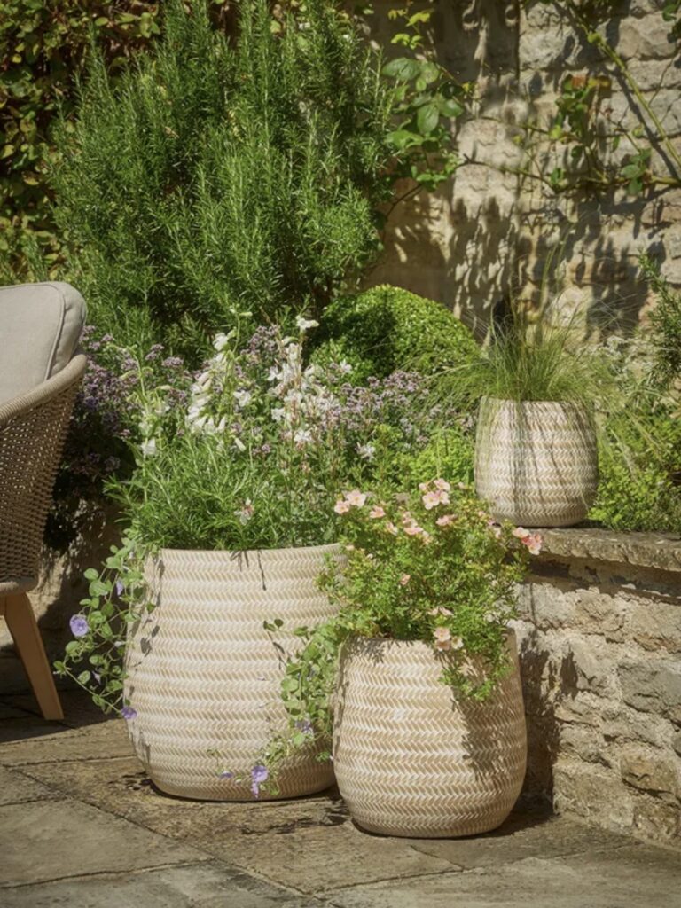 A stylish courtyard garden featuring Three Chevron Planters with lush greenery, ornamental grasses, and trailing flowers, offering elegant courtyard garden ideas for small outdoor spaces.