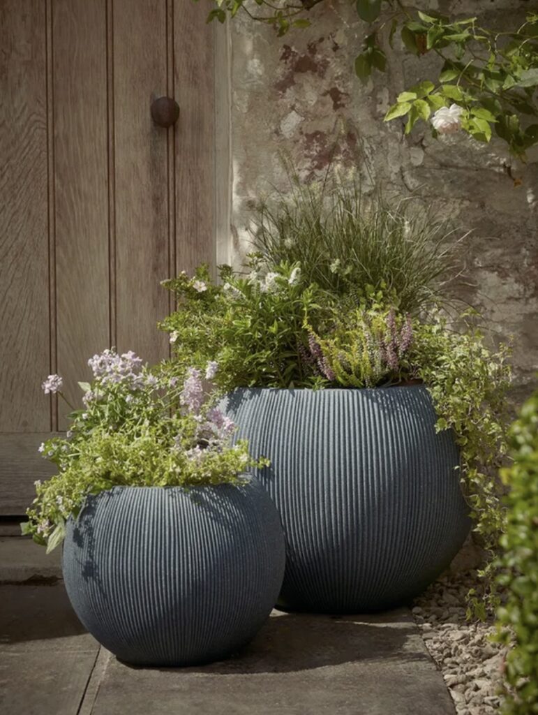 Two Fluted Dome Planters in anthracite, filled with ornamental grasses and trailing flowers, creating a modern focal point for rustic courtyard garden ideas