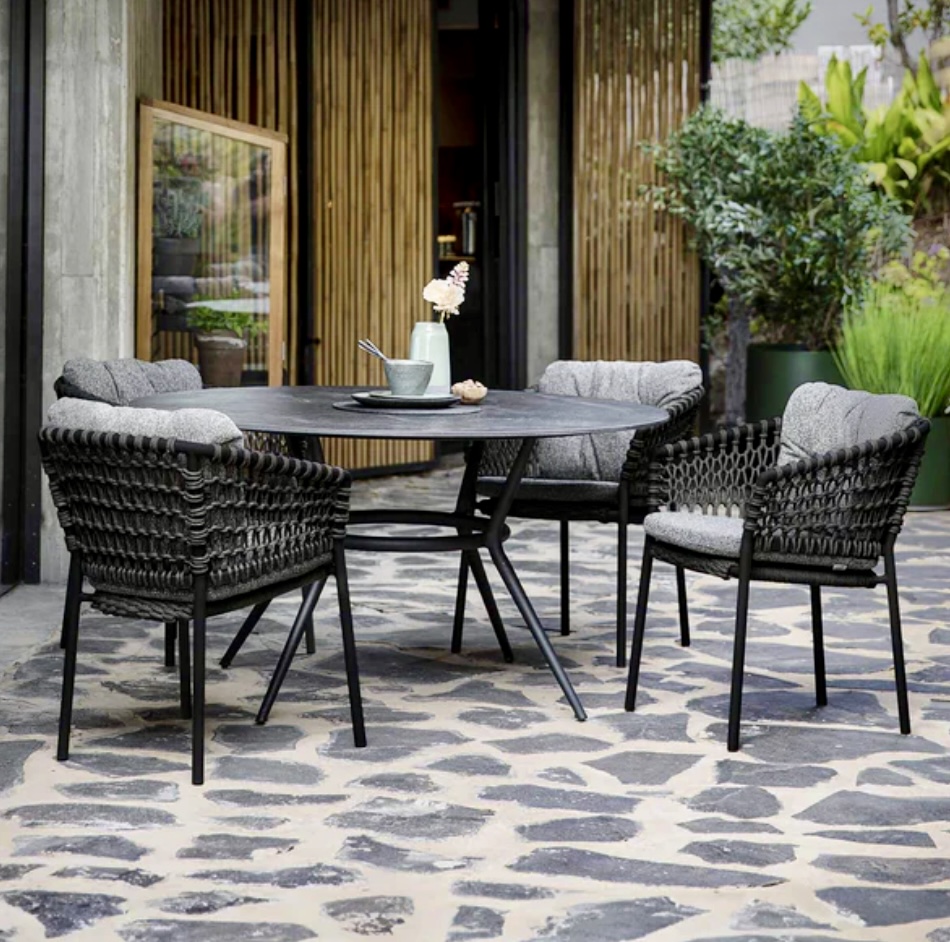 A modern courtyard garden with Cane-line Ocean Chairs and a sleek black dining table, set on geometric stone paving with lush greenery and bamboo screening, showcasing contemporary courtyard garden ideas.