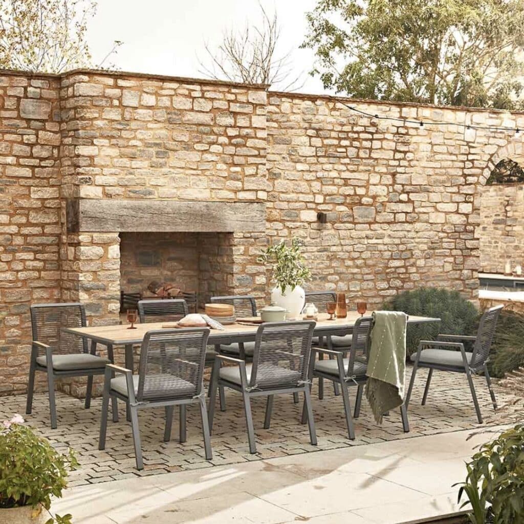 Atkin and Thyme Savannah extending outdoor dining set styled in a walled Dorset stone courtyard with cobble paving and outdoor fireplace.