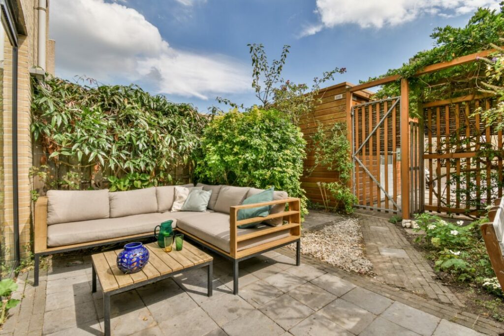Modern courtyard garden with a neutral-toned outdoor sectional sofa, wooden pergola, and lush greenery. A stylish and functional example of courtyard garden ideas for a cosy outdoor lounge space.