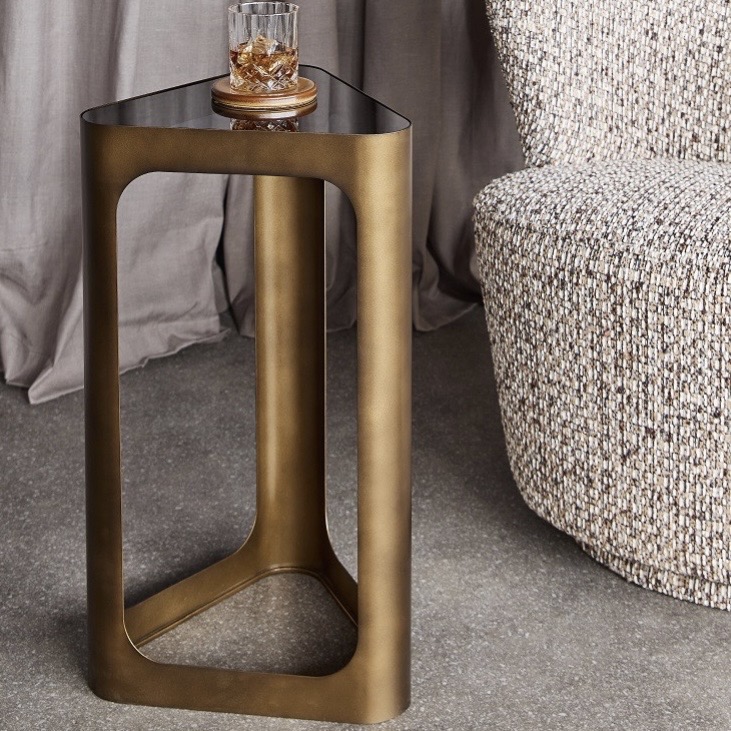 Unique side tables: Libra Thorpe triangular accent table with smoked gold metal frame and black tinted glass top beside an armchair.