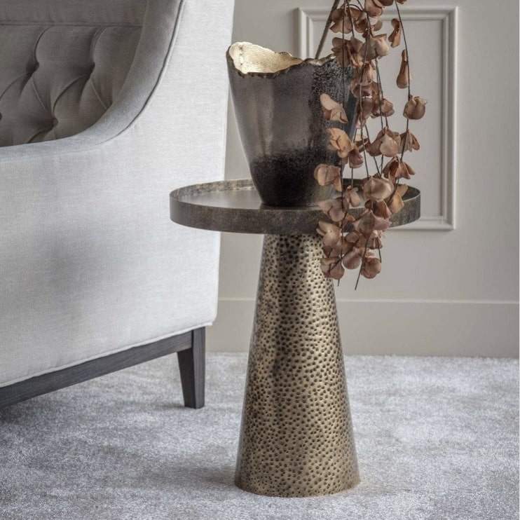 Sandbanks iron unique side table in rustic antique gold with hammered cone base beside an armchair.