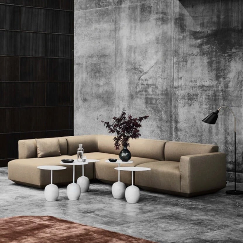 Stone unique side tables styled in a modern, minimalist living room with a concrete wall and low sofa, featuring the &Tradition LN9 Lato Oval Side Table with Emperador marble base and warm black top.