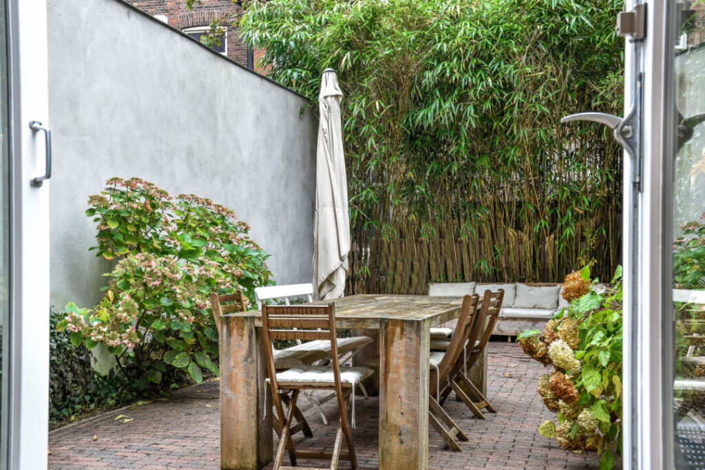 Rustic courtyard garden with a weathered wooden dining table, bamboo privacy screen, and lush greenery. A cosy and inviting example of courtyard garden ideas for outdoor dining and relaxation.
