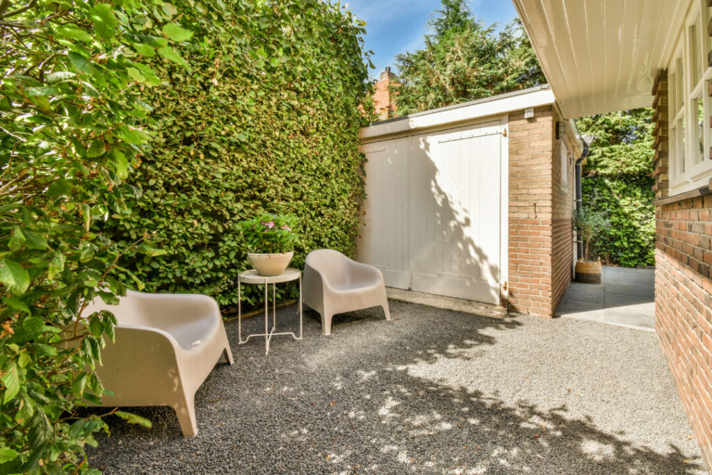 Minimalist courtyard garden with gravel flooring, modern outdoor chairs, and lush green privacy walls. A serene and stylish example of courtyard garden ideas for small outdoor spaces.