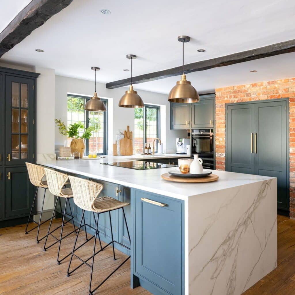 Blue kitchen island with brass pendant lights and rattan bar stools