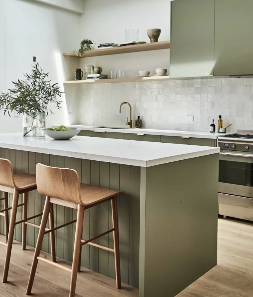 Sage green kitchen island with wood bar stools and open shelving