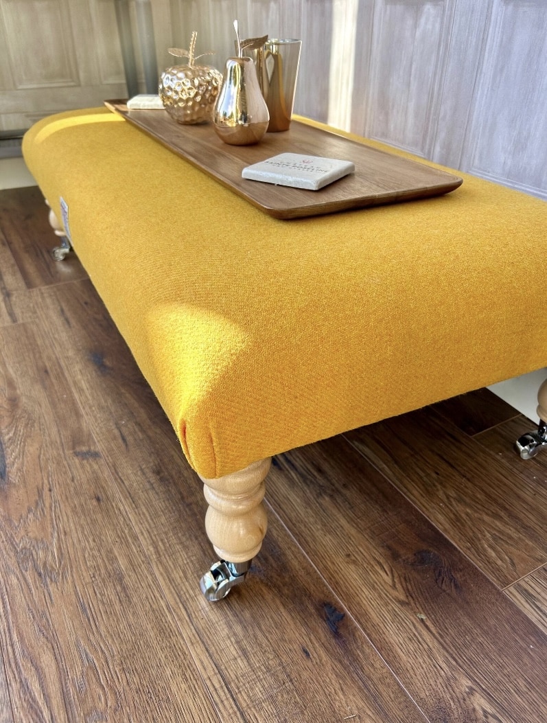 Ochre yellow Harris Tweed ottoman coffee table with wooden legs and castors, styled with a tray on top.