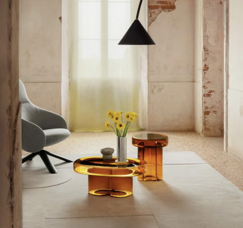 Amber glass Soda Oval colourful coffee table paired with matching side table in a modern living room featuring soft natural light, concrete walls, and yellow tulips.