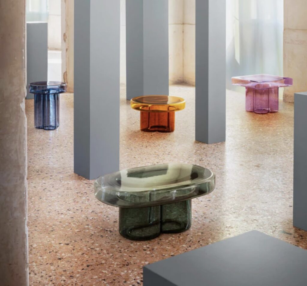 Collection of Miniforms Soda colourful coffee tables in blue, amber, lilac, and olive displayed in a gallery-style terrazzo room with sculptural columns.