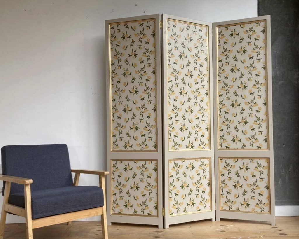 Three-panel folding screen with Farrow & Ball floral wallpaper in cream and olive green, painted wood frame, beside armchair