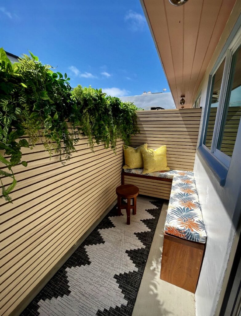 Faux greenery garland with bench seat and cushions – perfect for small balcony ideas focused on privacy and colour.