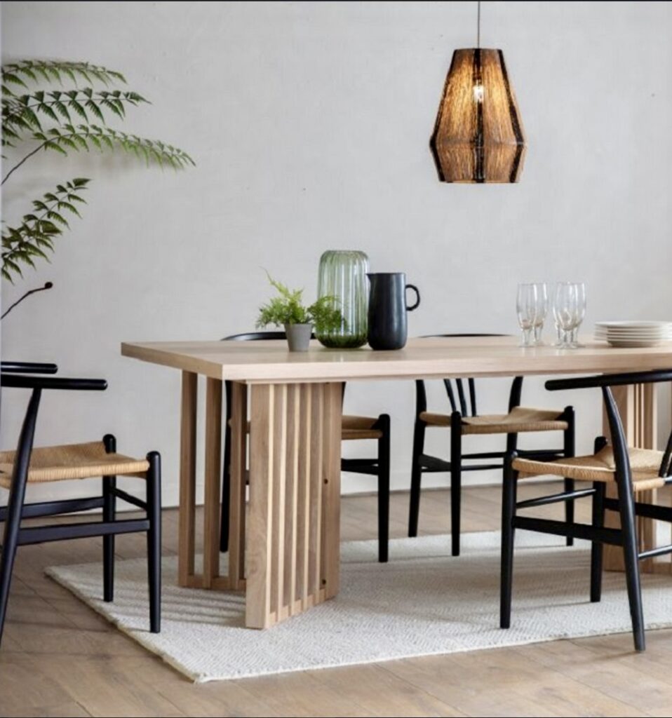 Kyoto Japandi style dining table with slatted oak legs and black framed dining chairs with woven seats, styled with glassware and greenery under a woven pendant light.