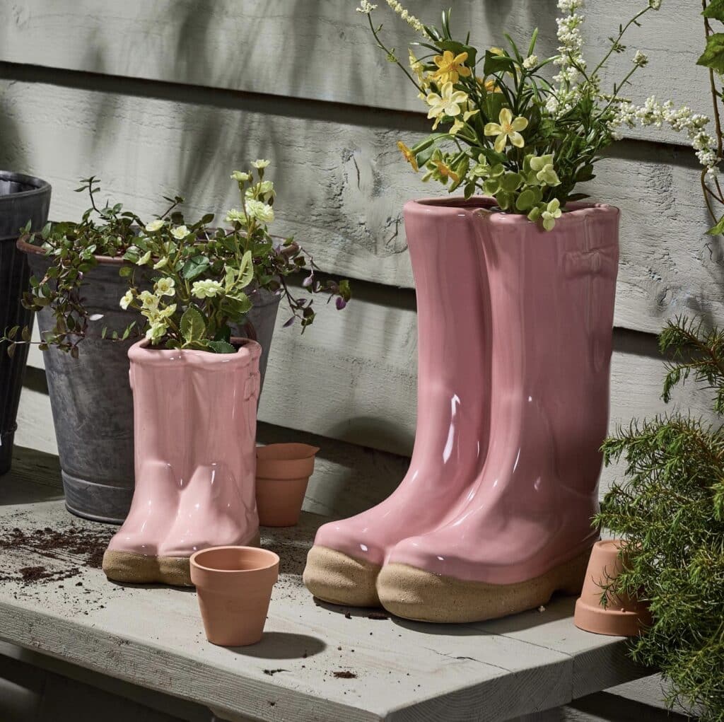 Pink ceramic welly boot planters on an outdoor shelf, styled with small plants and mini terracotta pots.