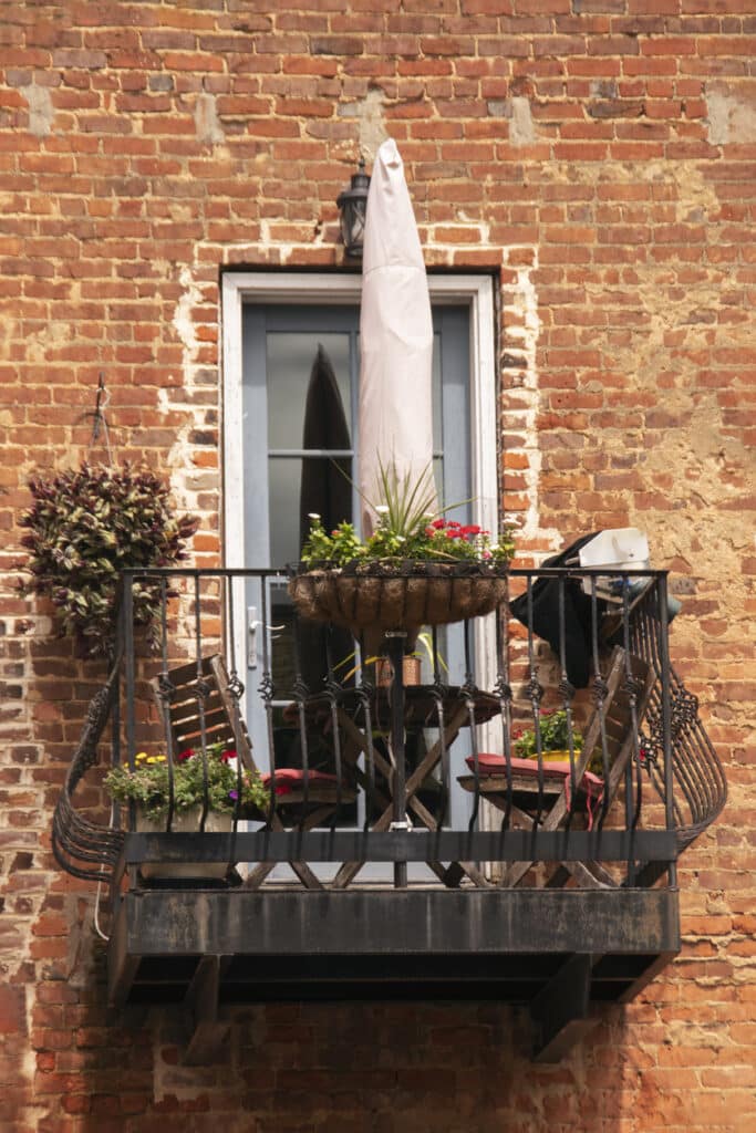 Very small balcony micro bistro set-up with compact table and chairs, balcony planters and a parasol for shade