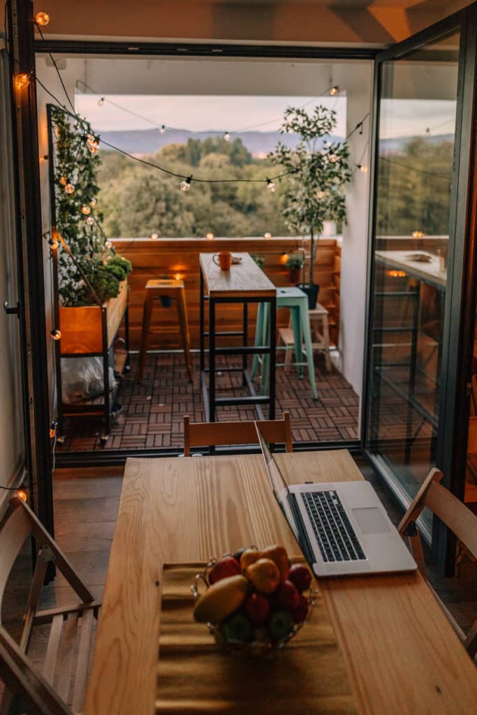 Small balcony ideas: a slim bar-height table with tuck-under stools, fairy lights and greenery creating a cosy apartment balcony seating spot.
