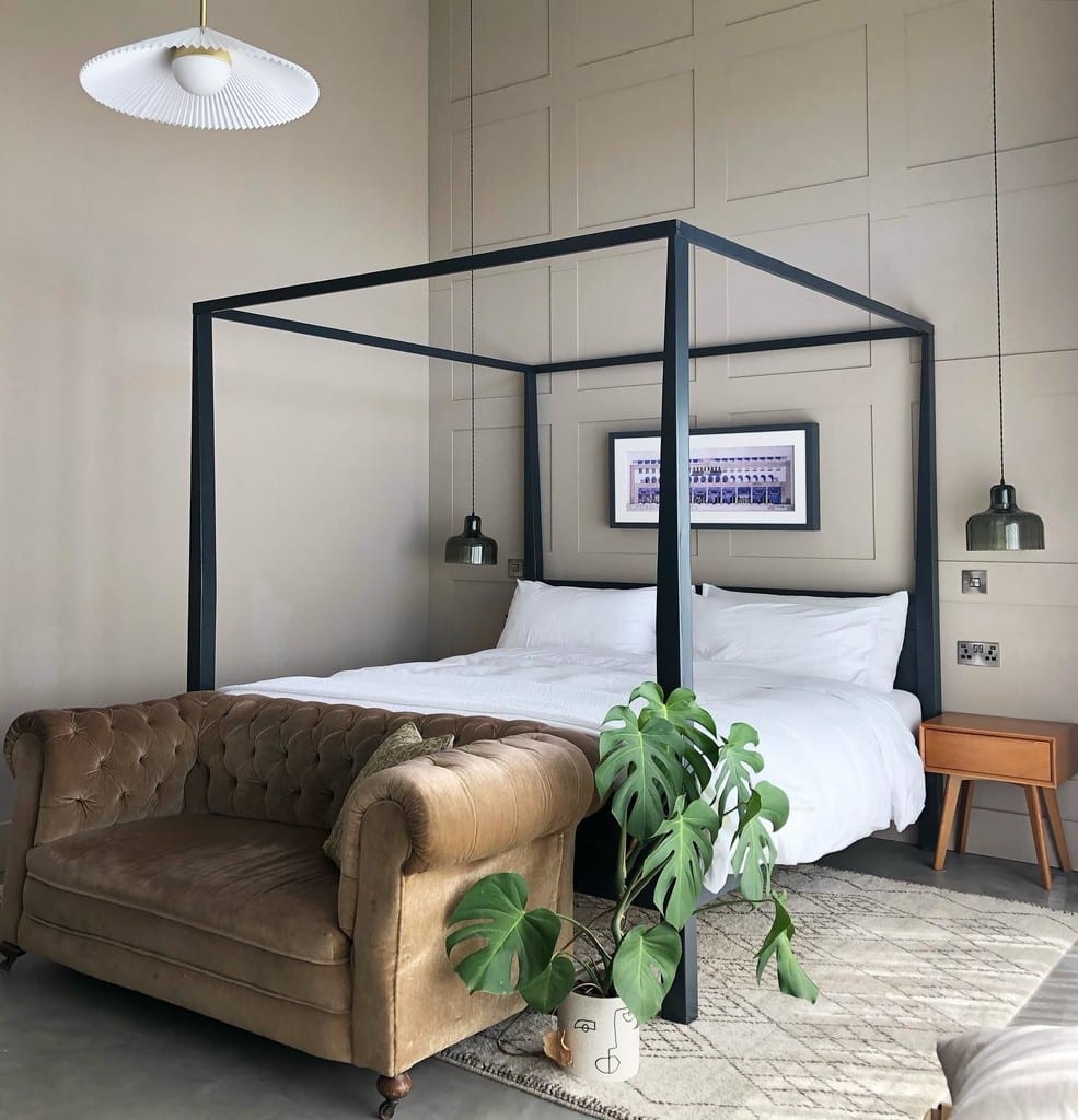 Black four-poster bed against beige panelled walls in a black and beige bedroom