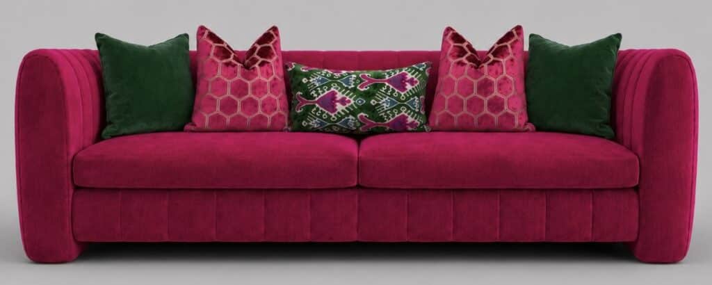 Fuchsia pink channelled velvet sofa styled with forest green velvet cushions, fuchsia hexagon geometric cushions and a pink and green ikat lumbar cushion for a bold, luxurious look