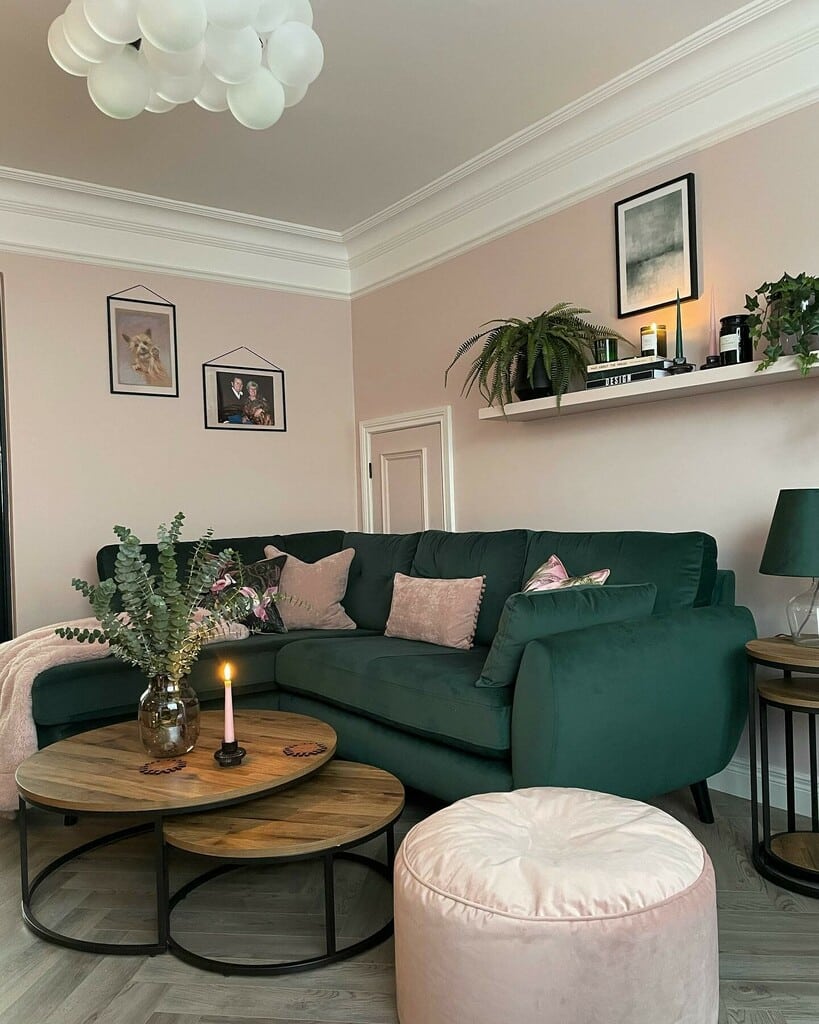 Pink and green living room with Calamine walls, dark green velvet corner sofa, pink cushions and pouffe, and wooden nested coffee tables