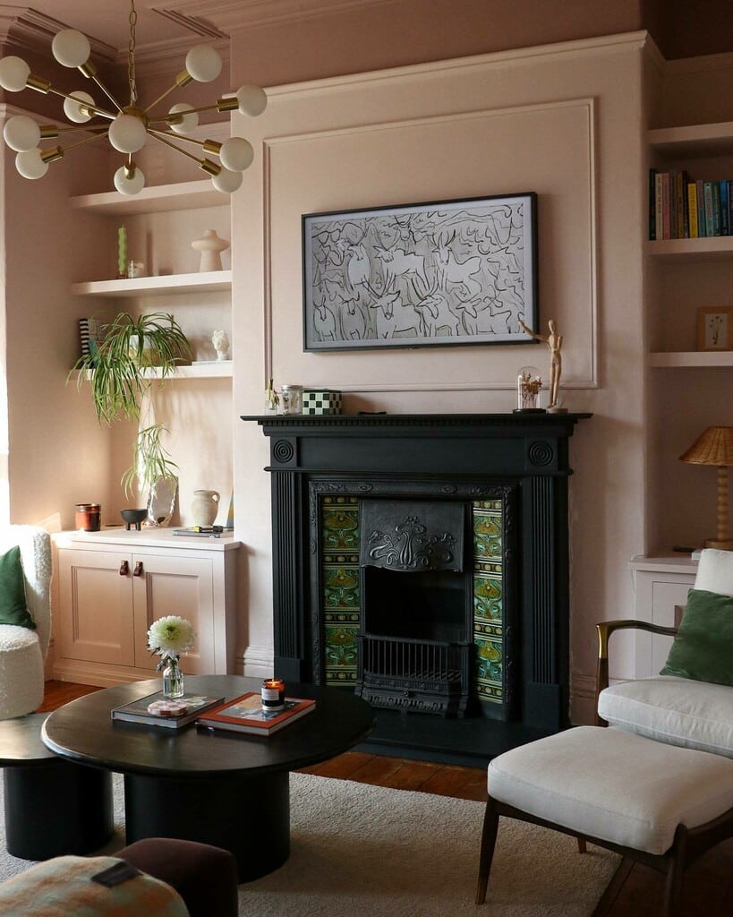 Pink living room with Calamine and Sulking Room Pink walls, black cast-iron fireplace with green patterned tiles, brass chandelier and green velvet chair accent