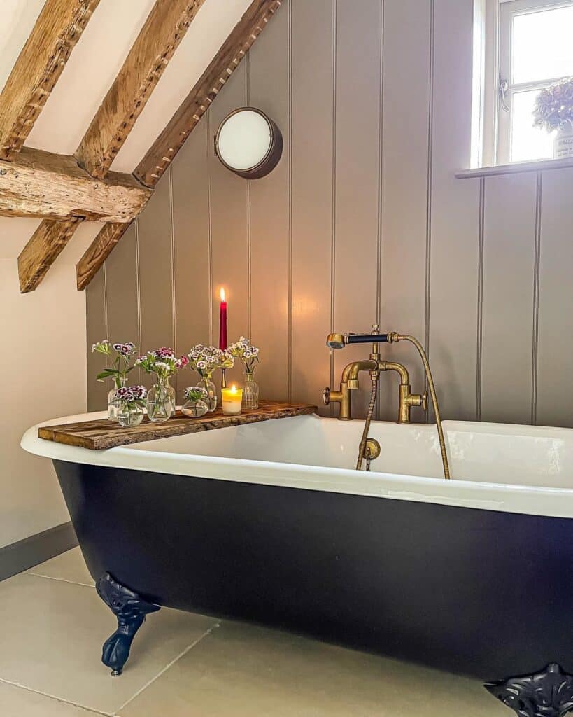 Rustic bathroom with exposed wooden beams, black roll top bath with brass fittings and Farrow and Ball Charleston Gray tongue and groove wall panelling