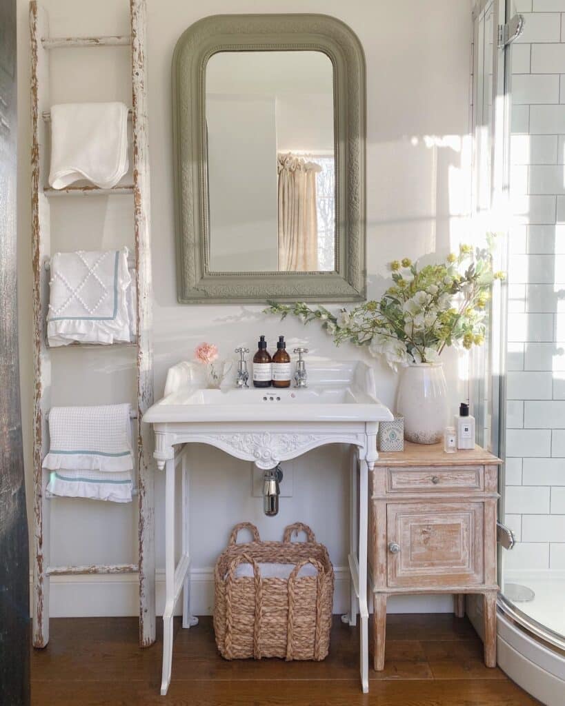 Rustic bathroom with Farrow and Ball Treron mirror frame, ornate white basin, vintage towel ladder and wicker basket