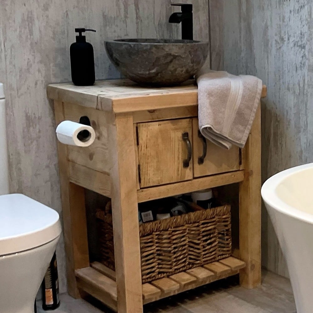 Compact rustic pine washstand with stone vessel basin, two-door cupboard and wicker basket shelf in a small bathroom