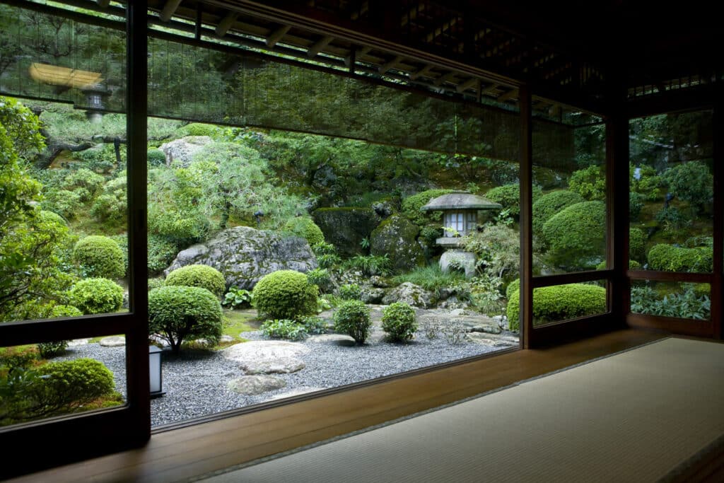 Traditional Japanese zen garden viewed from a tatami room, with cloud-pruned shrubs, raked gravel and a stone lantern