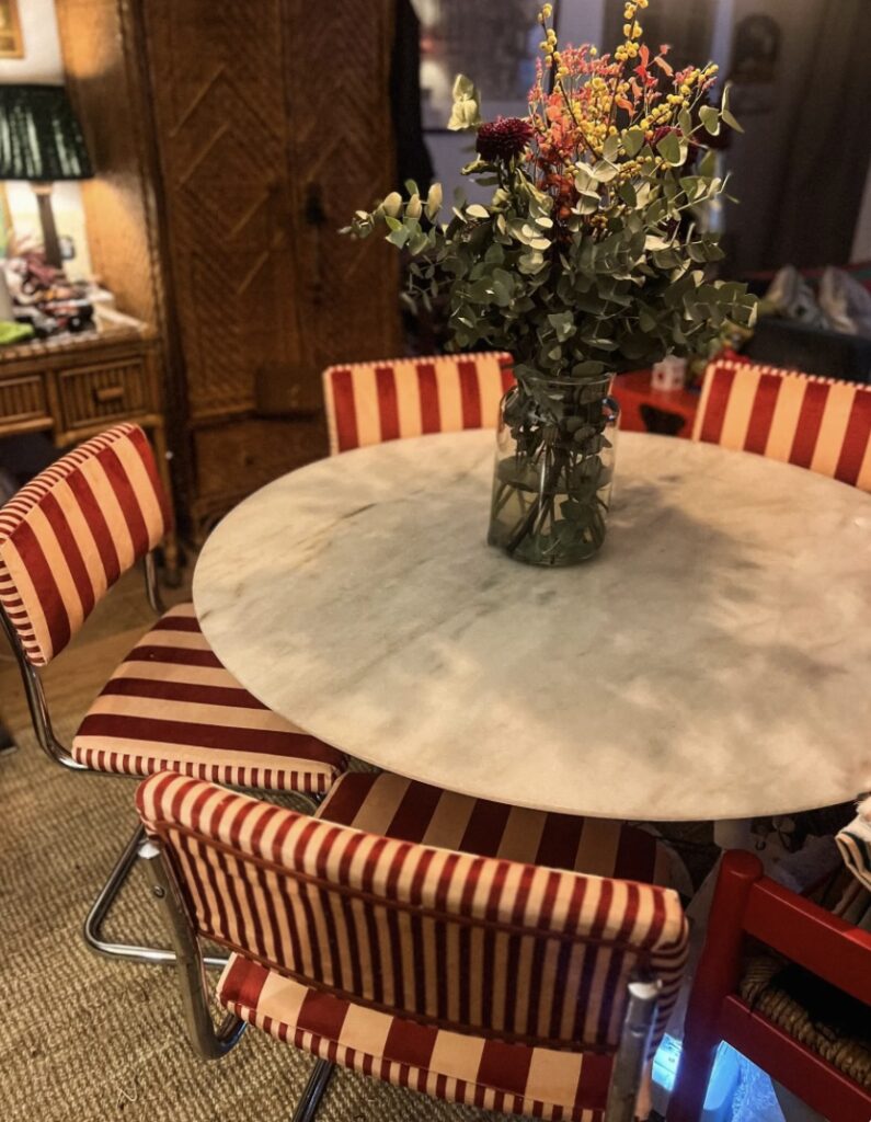 Dining table with vintage Cantilever upcycled dining chairs in red and cream striped velvet, styled with a round marble table and floral centrepiece for a retro-inspired look