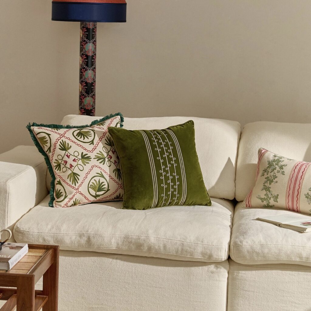 Beige sofa styled with olive green velvet and botanical print cushions for a warm, nature-inspired living room.