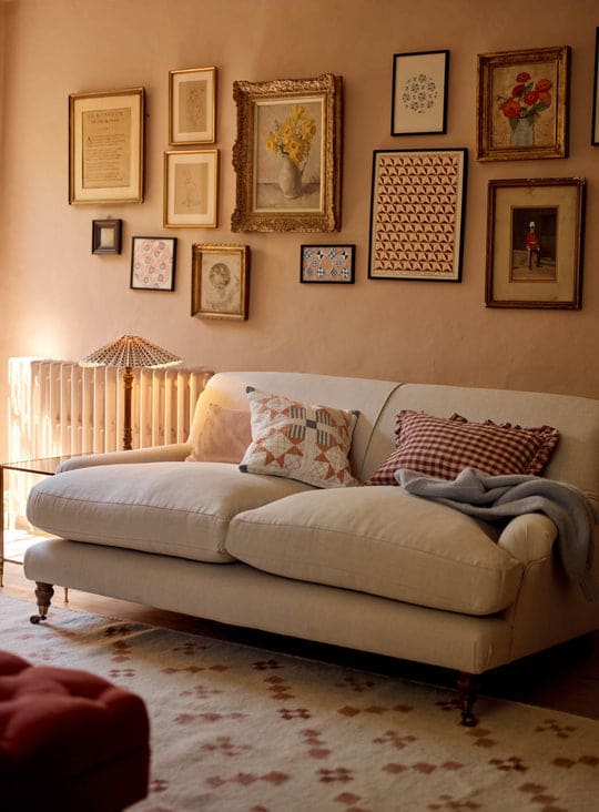Remy ecru linen sofa styled with patterned terracotta and ginghamu cushions, a rust ottoman, gallery wall and warm neutral décor.
