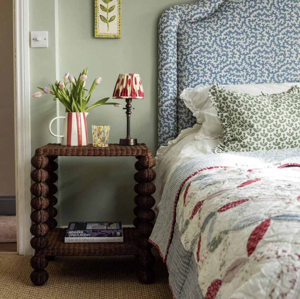 Cottage style bedroom with Bobbin Rattan Side Table (Teak), patterned upholstered headboard and layered bedding – cottage bedroom ideas.