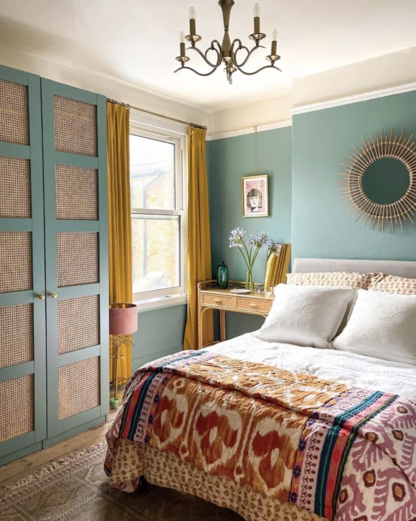 Oval Room Blue bedroom with cane wardrobes, mustard curtains and colourful patterned quilt.