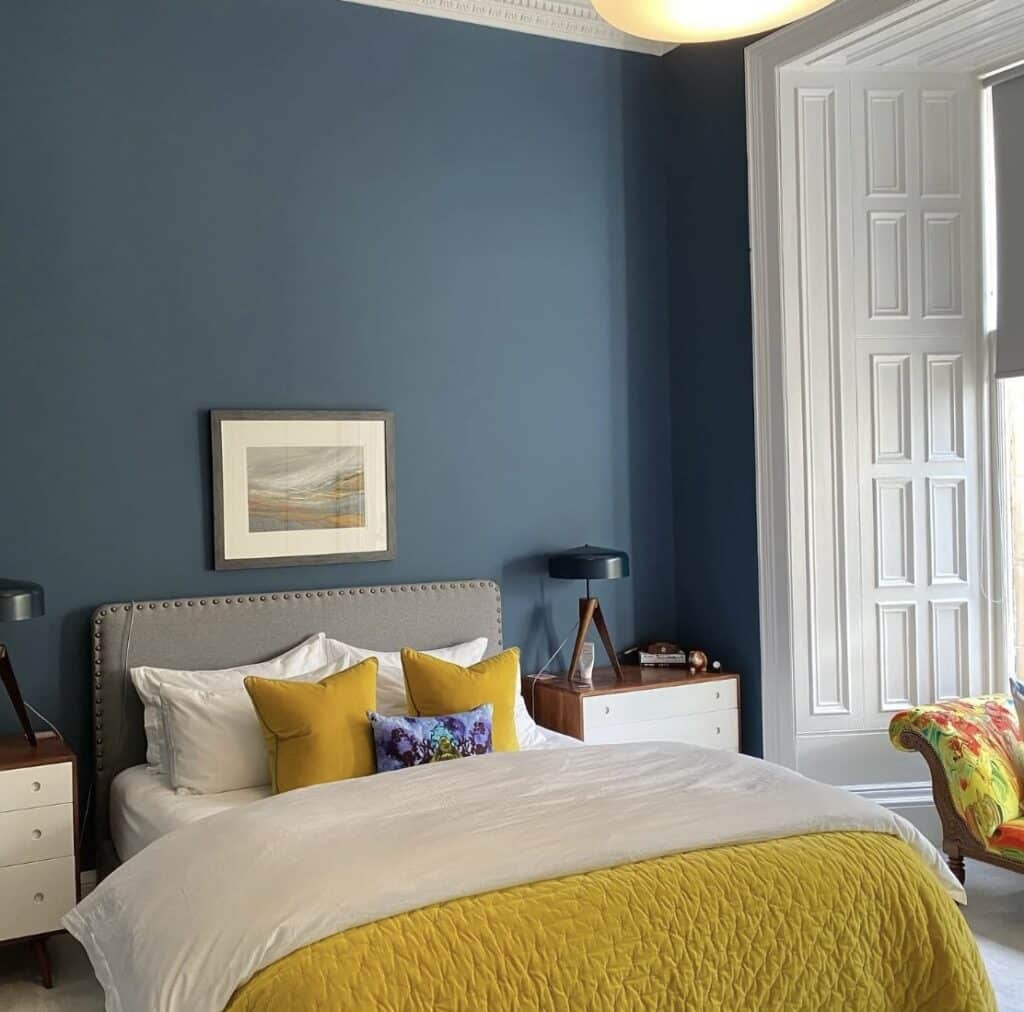 Blue bedroom ideas with deep navy walls, white bedding and mustard yellow cushions and throw for a romantic cosy navy blue bedroom