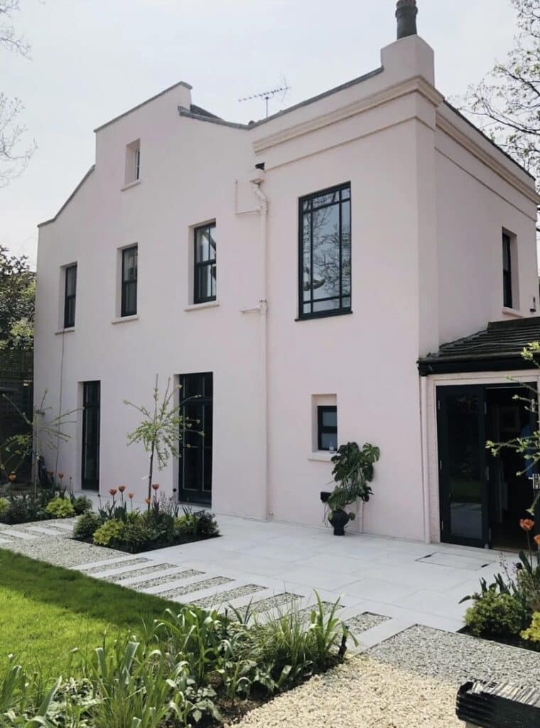 Gravel garden ideas for a modern home: pale gravel and crisp paving with a blush pink exterior and black-framed windows, creating a calm, low-maintenance front garden.