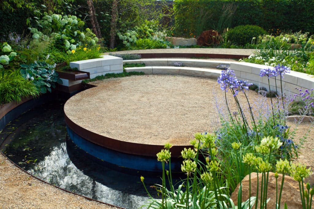Gravel garden ideas featuring a circular gravel seating area with curved steps, steel edging and lush planting.
