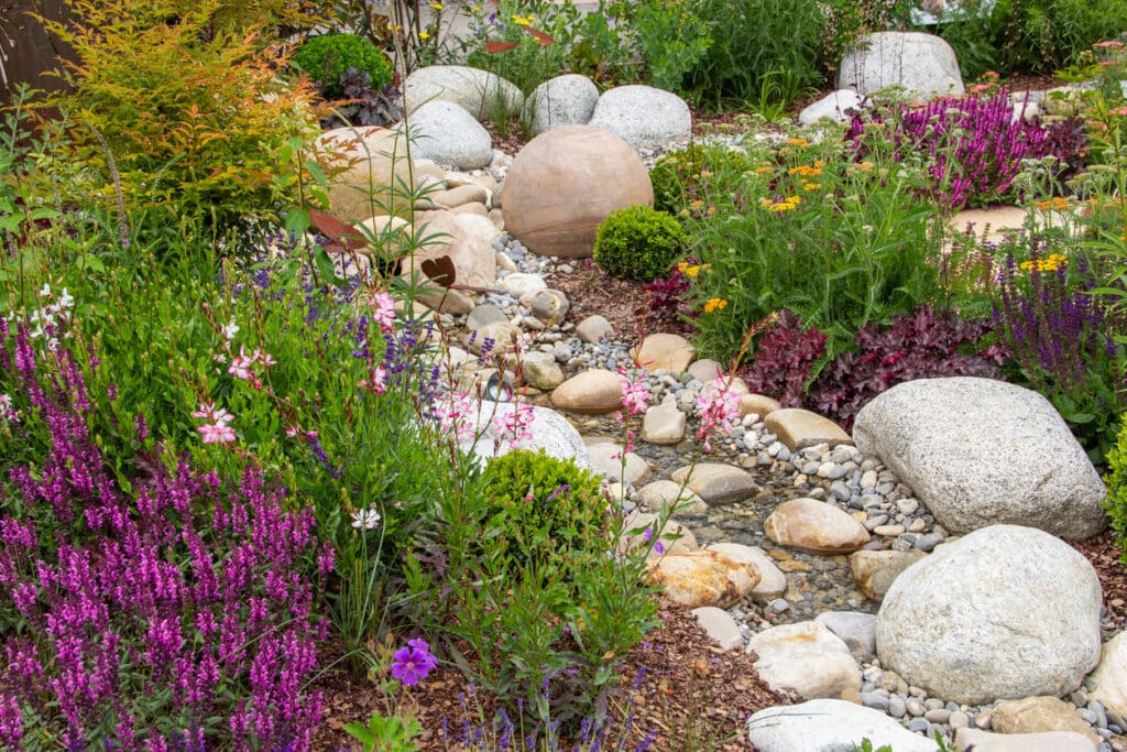 Gravel garden ideas showing a pond border with gravel, rocks and lush planting next to a paved seating spot