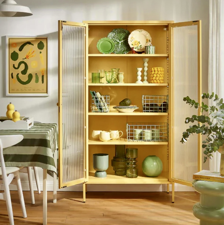 Mustard colour storage cabinet styled with green glassware, ceramics, and decorative accessories, set against a light, neutral-toned wall for a fresh and modern look.