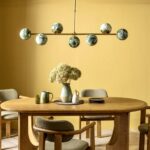 A stylish dining room featuring a wooden table, modern green and brass chandelier, and walls in a rich mustard colour.
