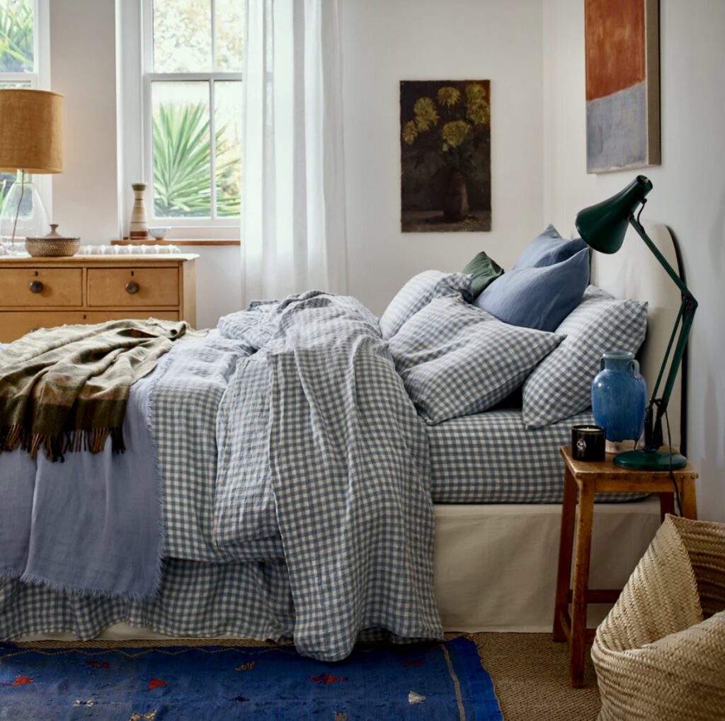 Cosy blue bedroom featuring a gingham check duvet cover, layered pillows, and warm wooden furniture. A charming cottage-inspired take on blue bedroom ideas with a soft, inviting feel