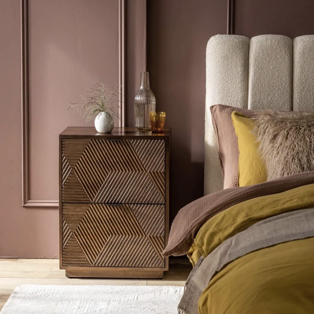 Bedroom with muted pink wall, mustard yellow bedding and a wooden bedside table
