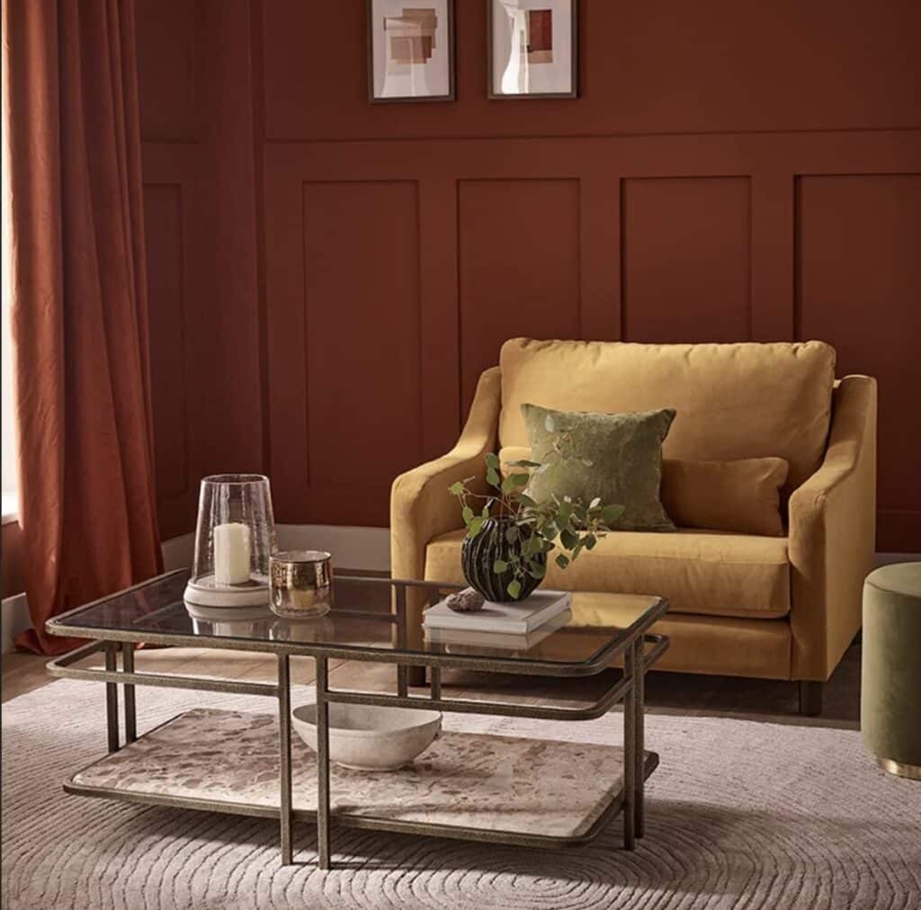 Mustard armchair with rust red panelled wall, terracotta curtains and a metal coffee table